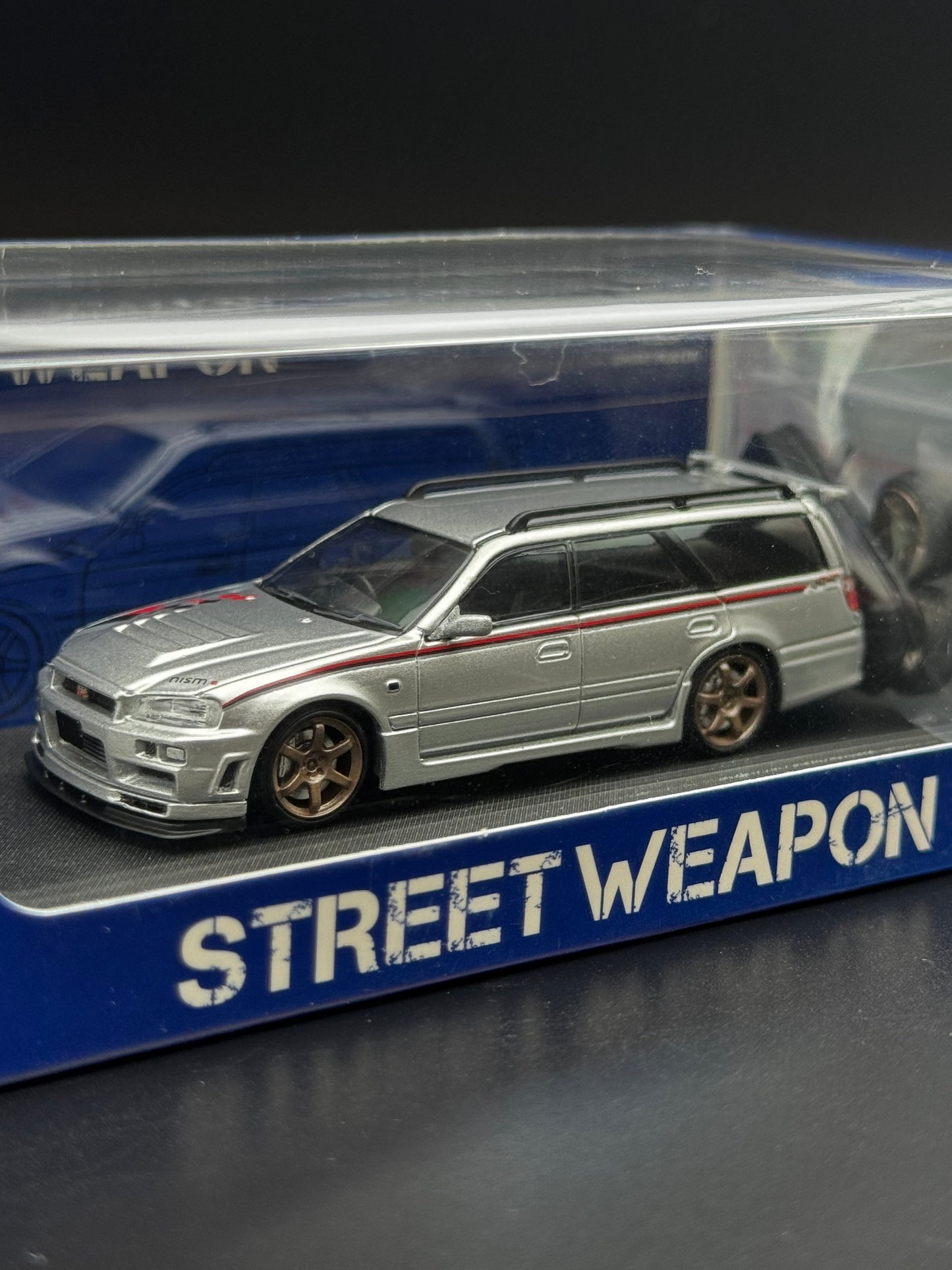 Nissan Stagea R34 Argent / Bande Rouge – Street Weapon 1/64 | 107/499 SVRdiecast